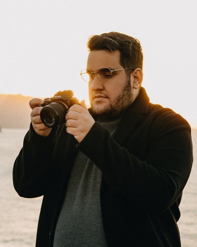 A man dressed in a black sweater with a camera
